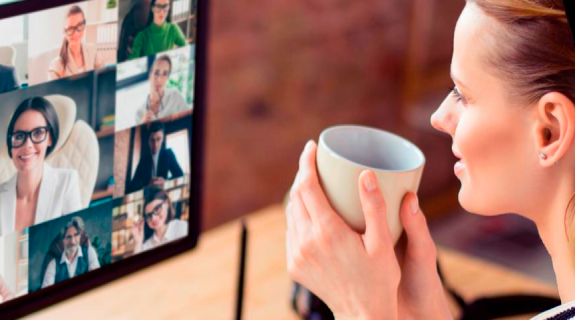 Eine Frau die vor einem Bildschirm sitzt und eine Kaffeetasse in den Händen hält.
