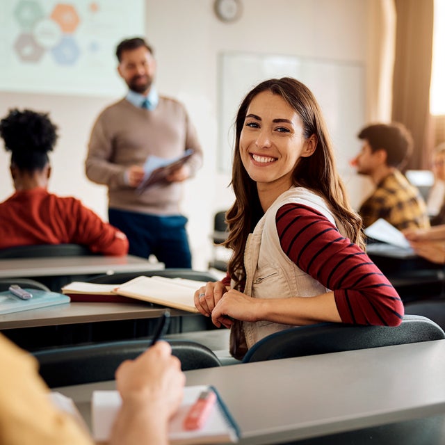 Classroom: In front is the teacher one female student looks directly into the camera