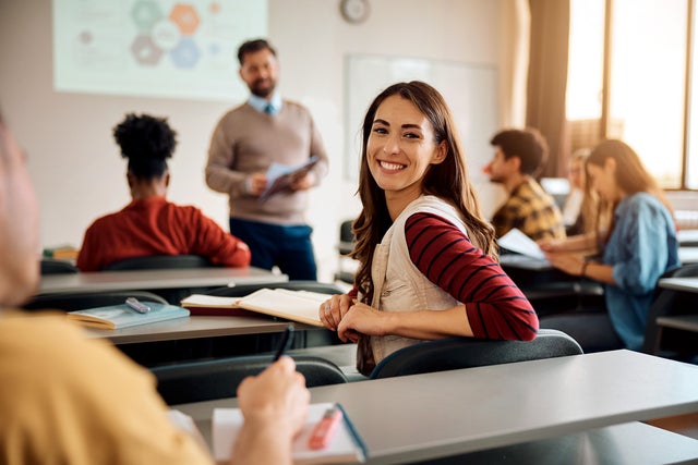 Classroom: In front is the teacher one female student looks directly into the camera