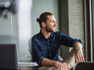 The Image shows a young man with a dark blue shirt, sitting relaxed on a table right by a window on the right side of the picture. He is smiling while looking outside, because with ista, his electricity billing is simplified and still precise, making it an effortless billing experience.