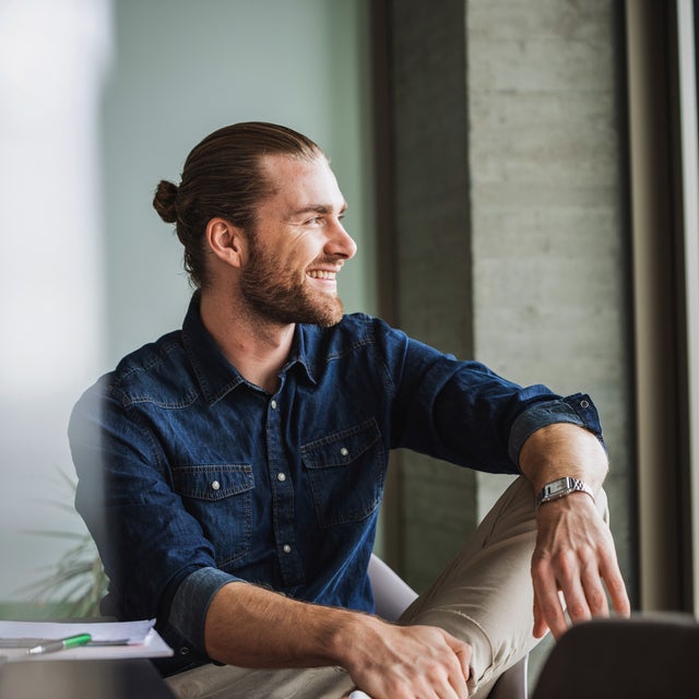 The Image shows a young man with a dark blue shirt, sitting relaxed on a table right by a window on the right side of the picture. He is smiling while looking outside, because with ista, his electricity billing is simplified and still precise, making it an effortless billing experience.