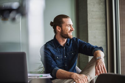 The Image shows a young man with a dark blue shirt, sitting relaxed on a table right by a window on the right side of the picture. He is smiling while looking outside, because with ista, his electricity billing is simplified and still precise, making it an effortless billing experience.