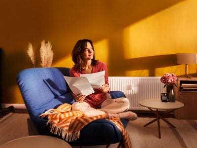 Eine Frau sitzt auf ihrer blauen Couch und blickt in die Ferne. In der Hand hält Sie die ista Heizkostenabrechnung. 